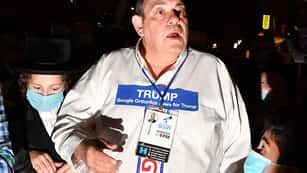 A photo of Heshy Tischler, an Orthodox Jew who lives in Brooklyn’s Borough Park. He is wearing a white pro-Trump shirt and there are masked people around him.